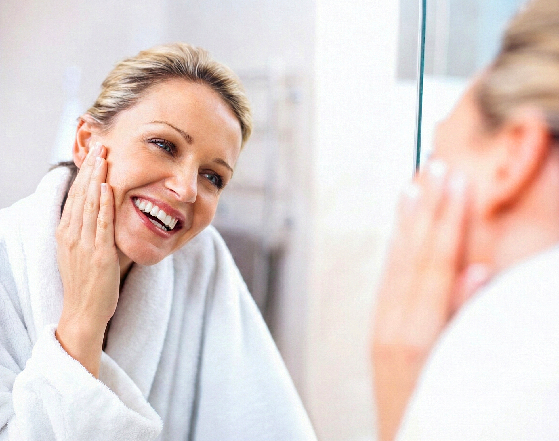 Woman in a white robe examining her face in a mirror